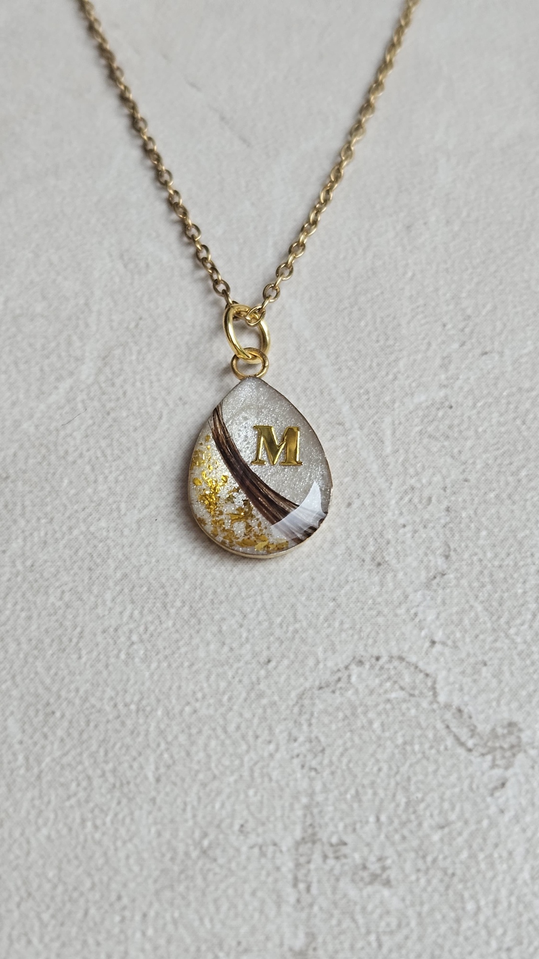 Tropfenförmiger Resin-Anhänger mit Tierfell, Blattgold und goldenem Buchstaben M an einer goldfarbenen Kette