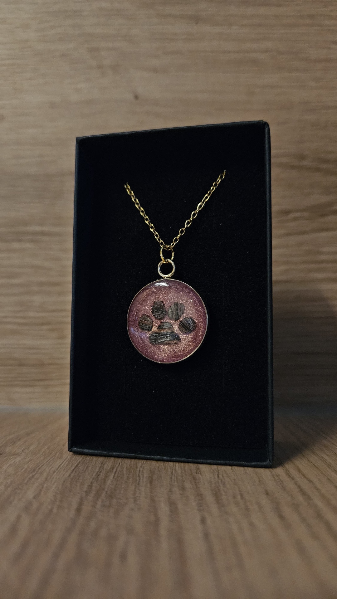 Roséfarbener Erinnerungsanhänger mit Pfotenmotiv in einer schwarzen Schmuckschachtel