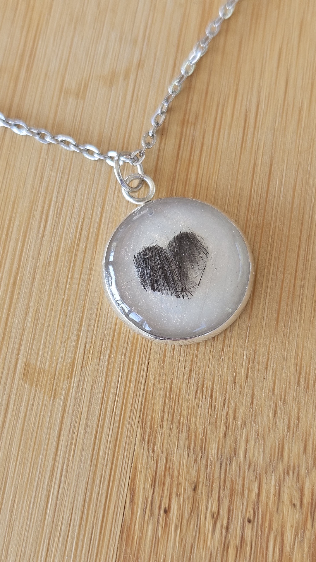 Heller Resin-Anhänger mit einem kleinen Herz aus Tierfell an einer silberfarbenen Kette