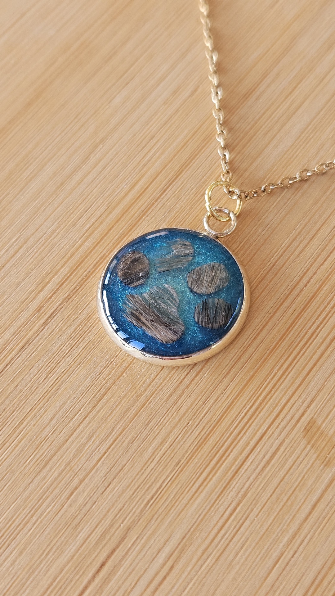 Blauer Resin-Anhänger mit einer Pfote aus Tierfell an einer goldfarbenen Kette